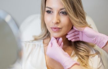 Beautiful fresh woman with clean skin of face and lips in beauty clinic. Professional woman cosmetologist doctor with pink gloves doing procedures