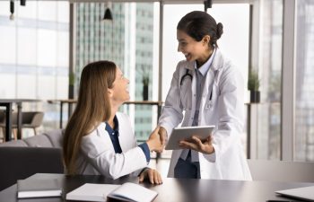 Gratitude for mentorship. Grateful young female medical worker intern shake hand of smiling woman expert mentor holding tablet pc appreciate for help support consultation assistance sharing knowledge