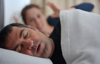 Woman (age 30) suffers from her male partner (age 40) snoring in bed. Noise concept. Real people. Copy space