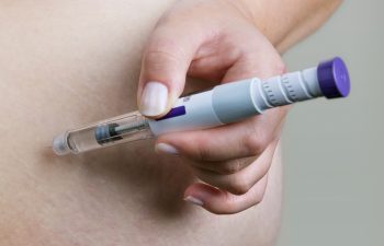 A person injects medication into their abdomen using an insulin pen.