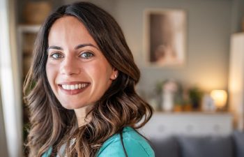 Female healthcare worker smiling, feeling happy and confident while wearing medical scrubs in a domestic setting, representing work-life balance and dedicated professional care