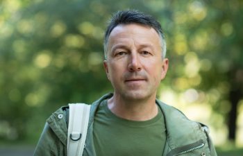 Handsome middle-aged man posing and looking at camera in autumn park over foliage. Outdoor male portrait. Male face close up.