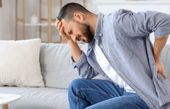 Young man suffering from back pain while sitting on sofa