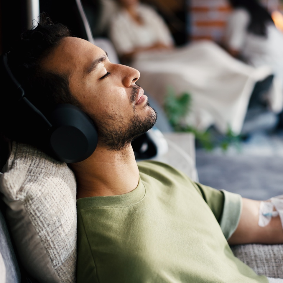 Man, sleep and iv drip with headphones for healthcare, iron infusion or immune booster in clinic. Male patient, rest or audio tech in medical lounge for intravenous solution, vitamin therapy or music.