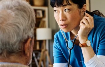 Doctor or nurse caregiver with senior man at home or nursing home using a stethoscope during an exam