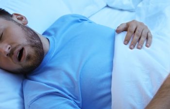 Young man snoring while sleeping in bed at night. Sleep disorder