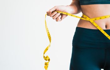 Close up shot of woman with slim body measuring her waistline and torso. Healthy nutrition and weight losing concept.