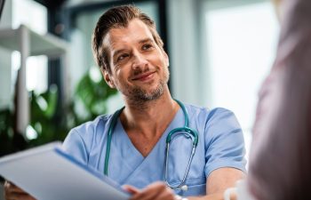 Happy doctor holding medical paperwork while communicating with patient during medical appointment at hospital.