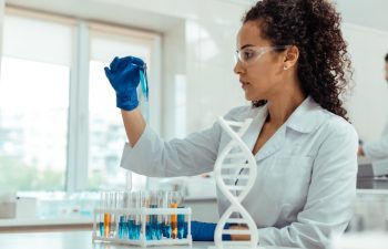 Scientific study. Nice young woman holding a test tube while looking at the blue liquid in it