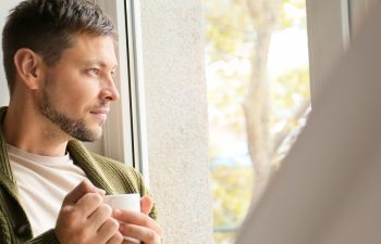 Man with cup of tea relaxing near window at home