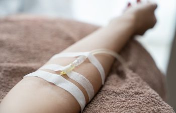 Patient with intravenous drip receiving saline solution. Injecting needle in to the arm.
