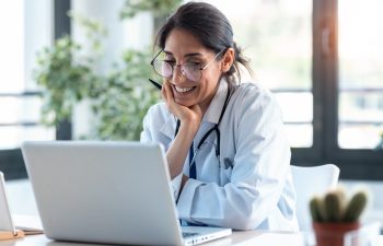 Shot of smiling female doctor working with her laptop in the consultation.