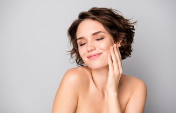Portrait of positive lovely pretty girl touch hand face enjoy her soft pure, perfect skin after bodycare plastic surgery treatment isolated over grey color background