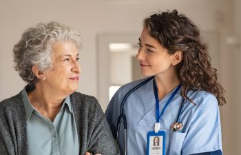 Young caregiver helping senior woman walking. Nurse assisting her old woman patient at nursing home. Senior woman with walking stick being helped by nurse at home.