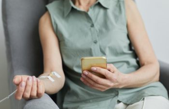 Minimal close up of unrecognizable woman getting IV drip and using smartphone, copy space