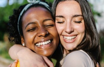 Candid happy multiracial best women friends embracing outdoors - Close up view of two diverse girls hugging each other with closed eyes smiling - Female friendship