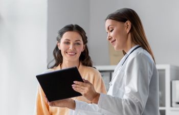 medicine, healthcare and people concept - female doctor with tablet pc computer talking to smiling woman patient at hospital