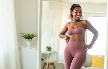 Successful weight loss concept. Happy slim african american woman in sports clothes looking at her reflection in mirror and smiling, feeling satisfied with slimming