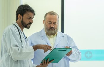 banner of Two senior doctor hold clipboard document file of patient record talking discussion about treatment guidelines. Men surgeon doctor advice assistance expertise for comprehensive care team.