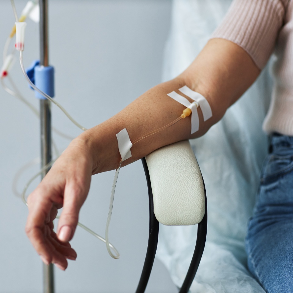Closeup of female hand with IV drip infusion in treatment session at hospital, copy space