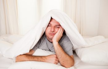 young man in bed with eyes opened suffering insomnia and sleep disorder thinking about his problem