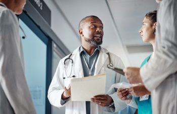 Hospital, teamwork and doctor with folder, conversation and brainstorming for healthcare and administration. Medical, leader and senior professional with group and meeting with documents and clinic.
