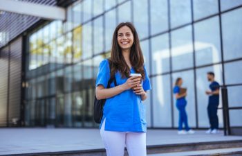 Confident nurse on her way to work in a clinic. Pretty female nurse drinking coffee and rest after hard work. The young adult female nurse drinks her coffee as she arrives to work at the hospital.