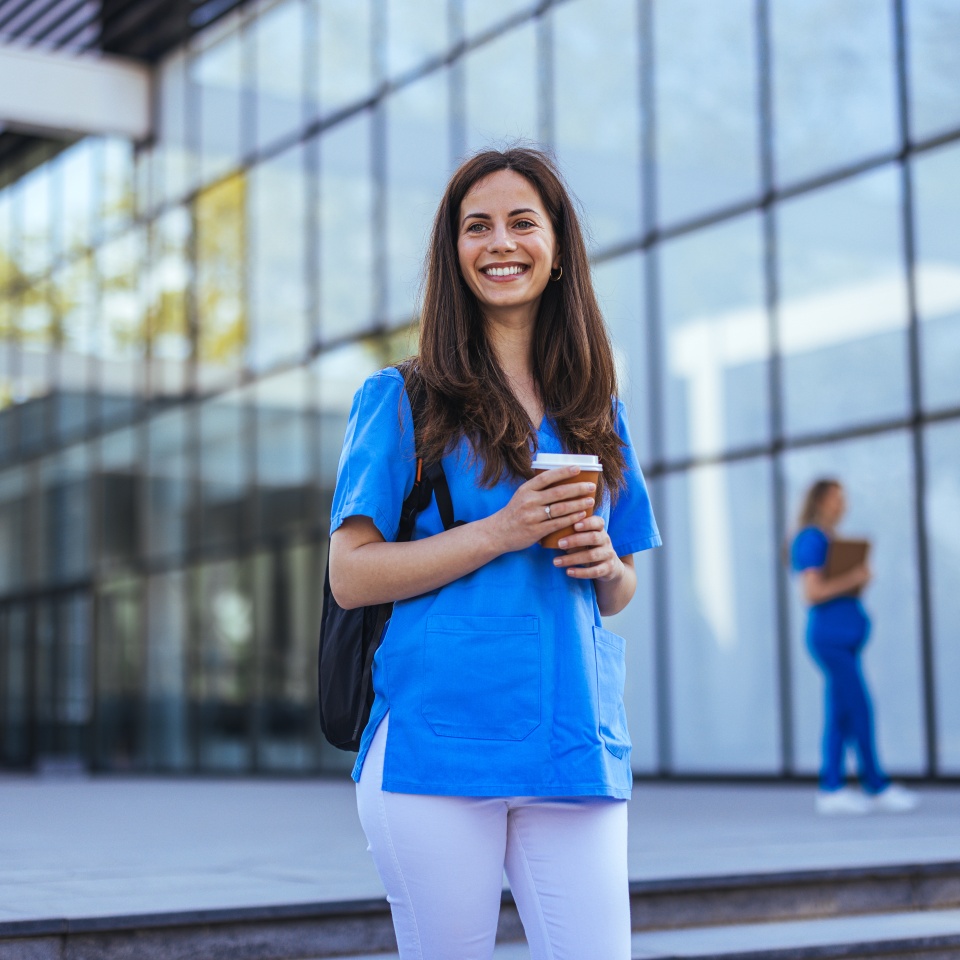 Confident nurse on her way to work in a clinic. Pretty female nurse drinking coffee and rest after hard work. The young adult female nurse drinks her coffee as she arrives to work at the hospital.