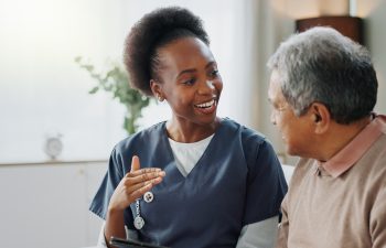 Nurse, senior and consulting with tablet on sofa for healthcare, communication or consultation at home. Woman or medical caregiver talking to elderly male person with technology for advice or help.