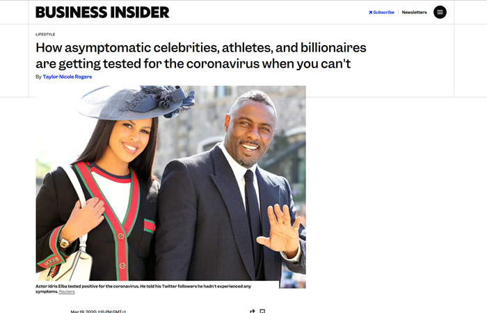 Two people dressed formally stand together and smile for the camera, one of them waving; the headline discusses coronavirus testing accessibility.
