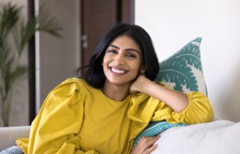 Portrait of happy Indian woman relaxing on comfortable couch, leaned on cushion, laughing, stare at camera, exuding satisfaction, enjoy pleasant, carefree daytime rest, weekend alone at modern home