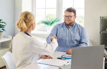 Doctor and patient consultation ends with handshake. A friendly clinician gives advice on weight loss, nutrition and healthier habits. Successful healthcare partnership and motivation.