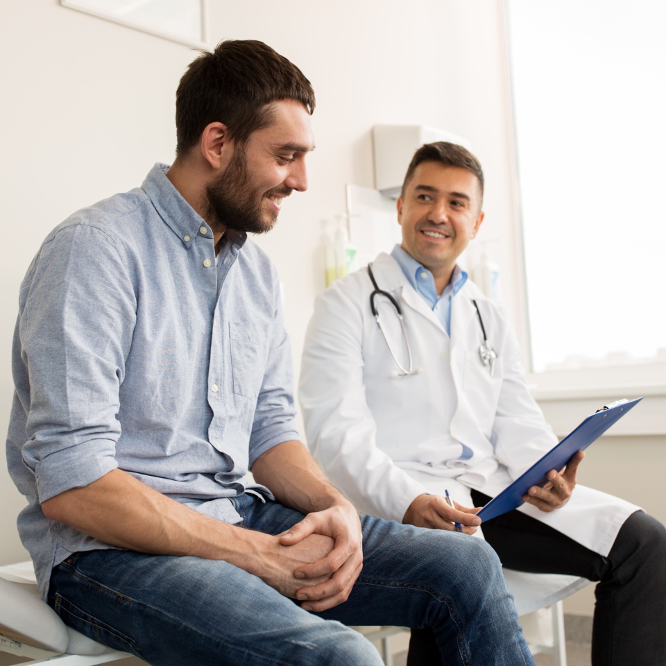 medicine, healthcare and people concept - smiling doctor with clipboard and young man patient meeting at hospital