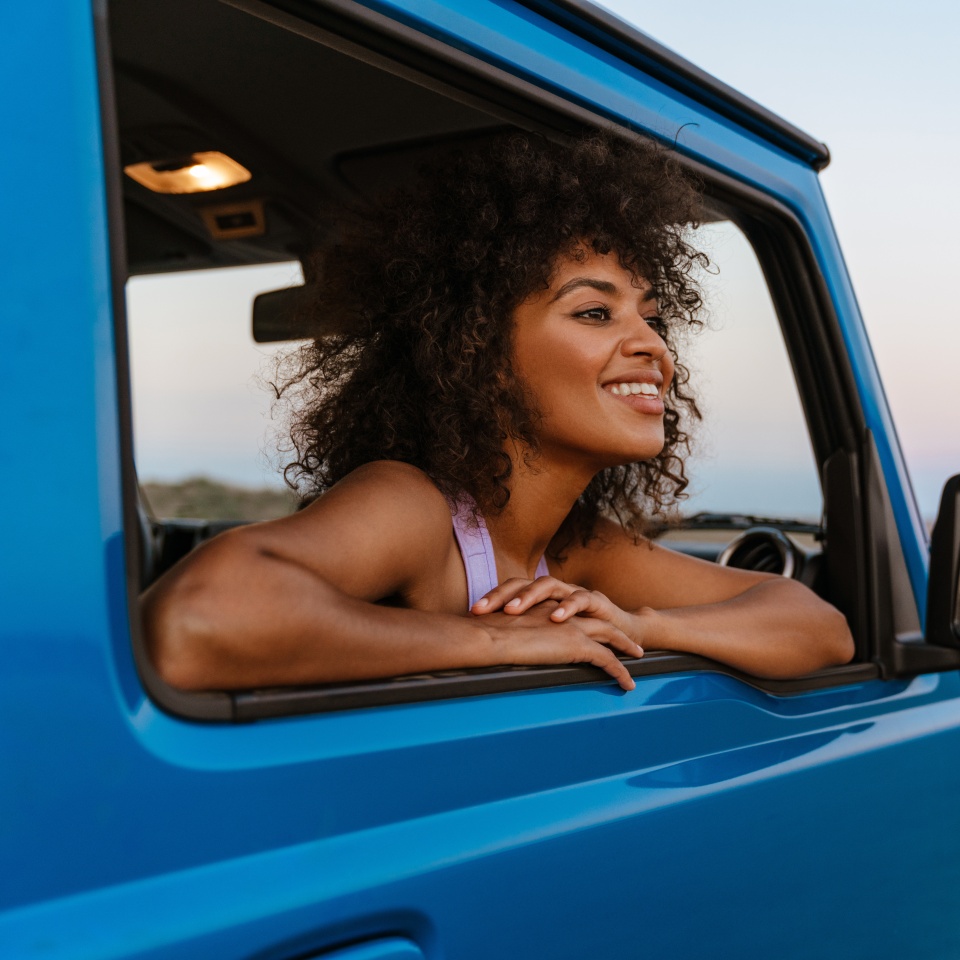 Image of cheerful african american woman smiling while travelling in car on desert