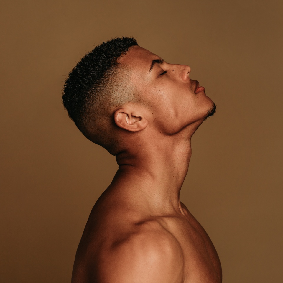 Close up of muscular man on brown background with face facing up. Portrait of shirtless african american fit man.