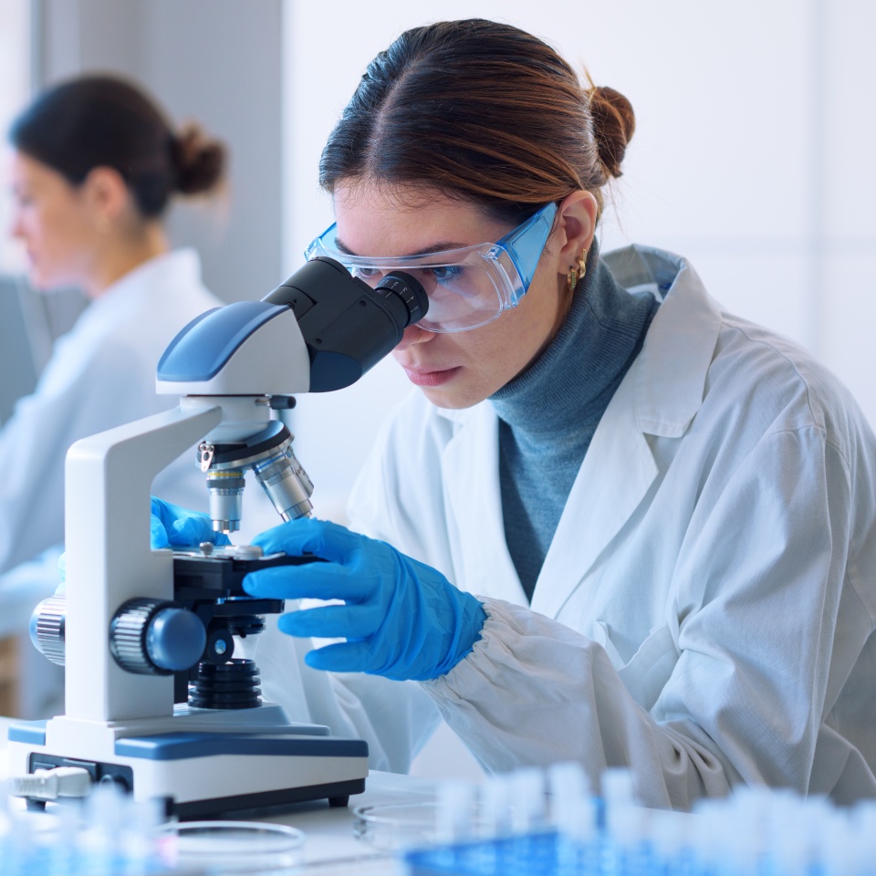 Young scientists conducting research investigations in a medical laboratory, a researcher in the foreground is using a microscope