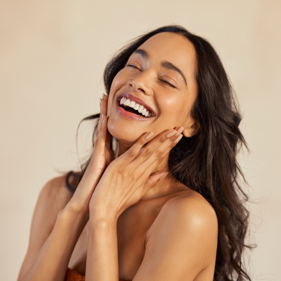 Multiethnic young woman touching her clean and healthy face against background with closed eyes. Latin hispanic woman feeling good with perfet skincare routine. Natural beauty portrait of mexican girl with black long hair.