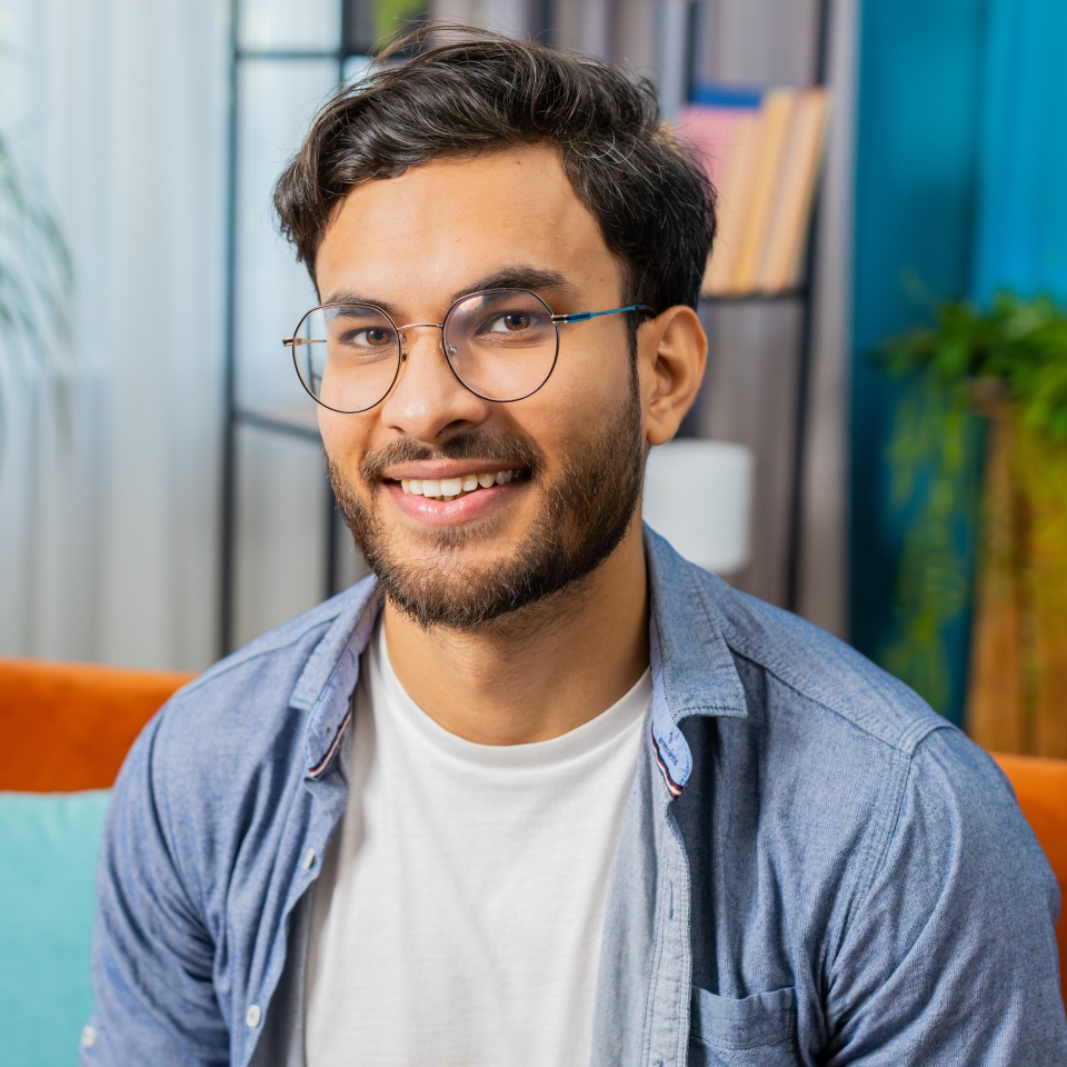 Portrait of happy calm Indian Arab man at home couch smiling friendly glad expression looking away dreaming resting relaxation feel satisfied good news celebrate win. Arabian young guy in living room
